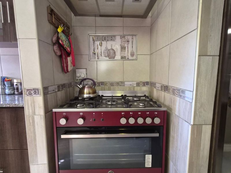 A compact kitchen cooking station featuring a modern red gas stove, oven, and stainless steel extractor fan set within a tiled alcove.