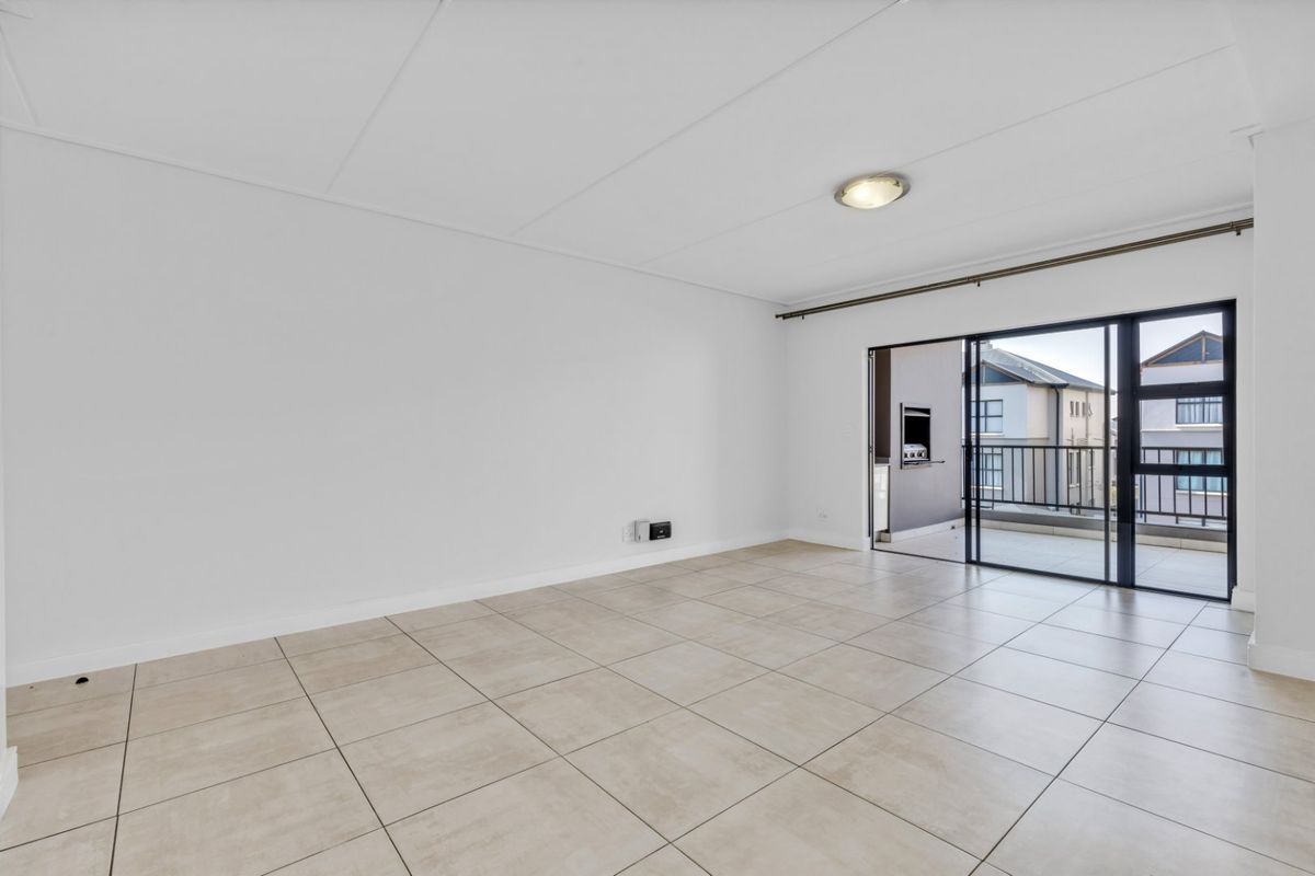 A bright, open-plan living area featuring neutral tiled flooring and large sliding glass doors that provide seamless access to an outdoor balcony.