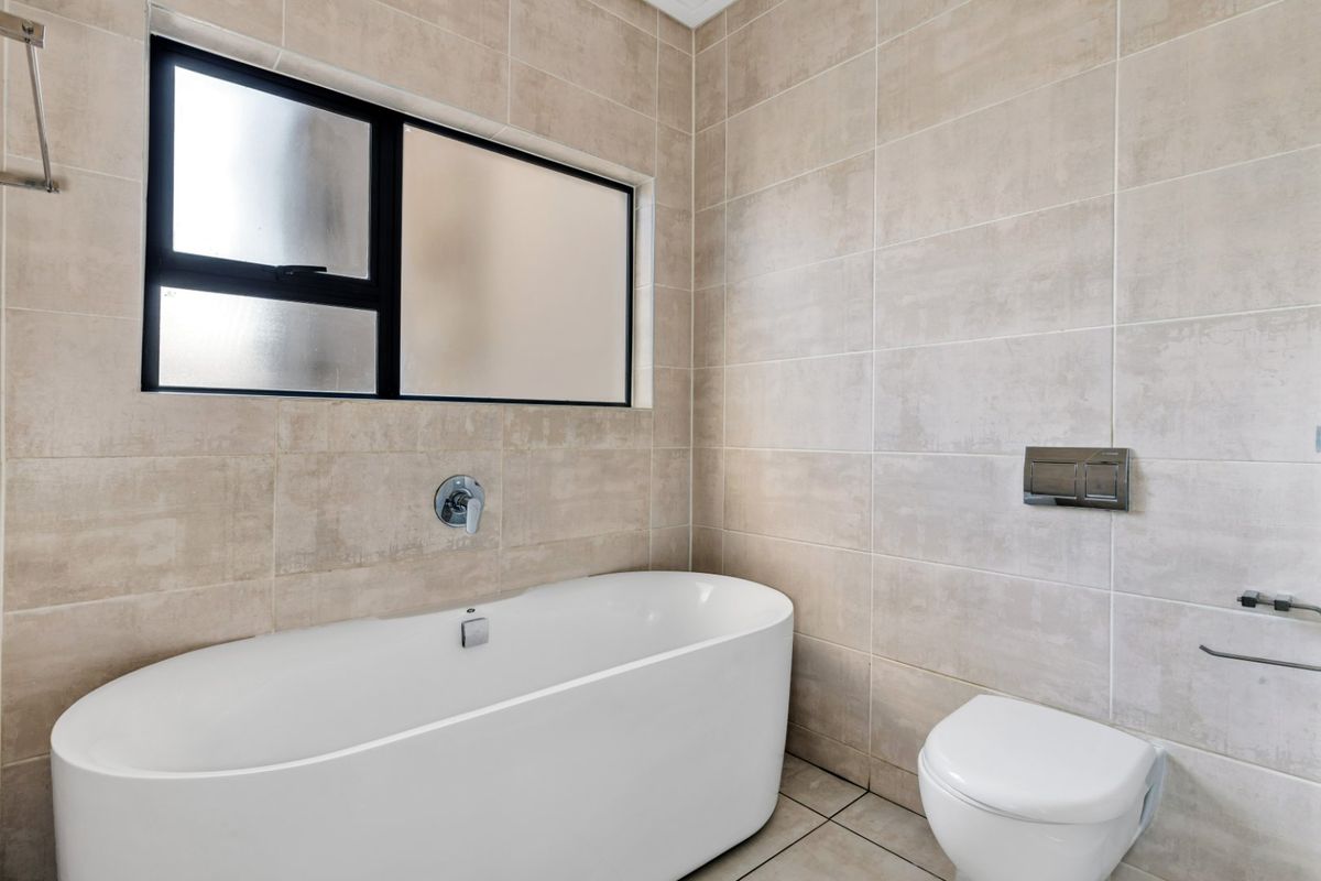 Modern bathroom featuring a sleek freestanding bathtub, wall-mounted toilet with concealed cistern, and neutral floor-to-ceiling tiling.