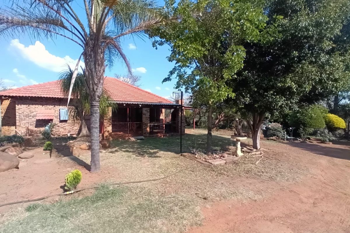 A view of the rear exterior of the farm property, featuring a face brick facade, tiled roof, and a covered patio area surrounded by mature trees.
