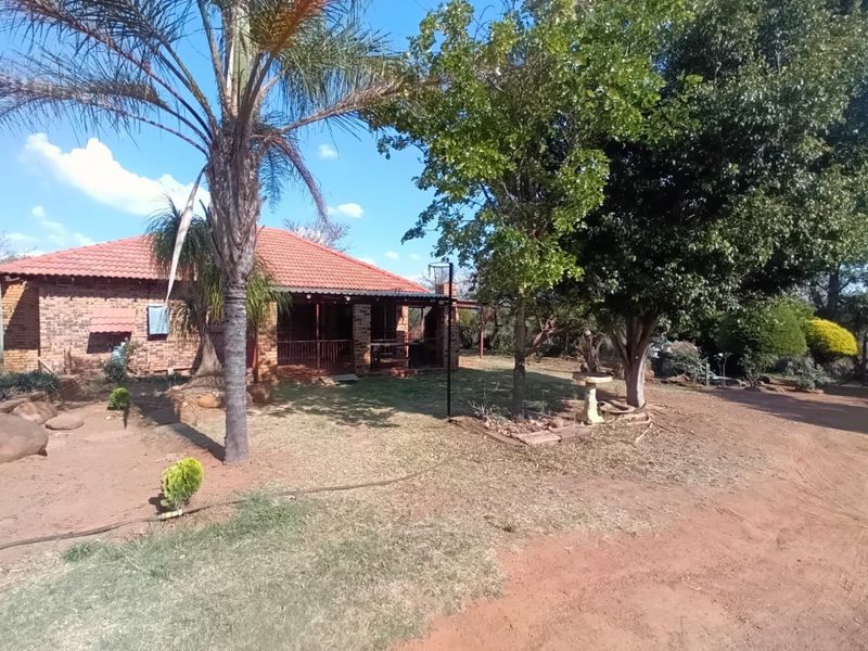 A view of the rear exterior of the farm property, featuring a face brick facade, tiled roof, and a covered patio area surrounded by mature trees.