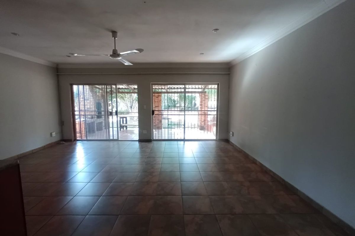Spacious, empty living area featuring tiled flooring, a ceiling fan, and large sliding glass doors that provide access to the outdoor patio area.