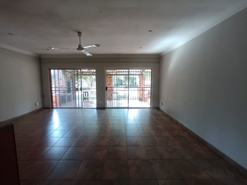 Spacious, empty living area featuring tiled flooring, a ceiling fan, and large sliding glass doors that provide access to the outdoor patio area.