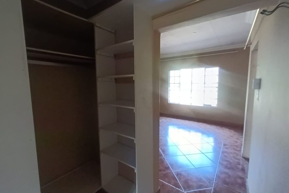 An empty bedroom featuring built-in wardrobe storage, tiled flooring, and a grid-pattern window allowing natural light into the space.