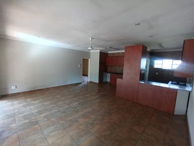 Spacious open-plan living and kitchen area featuring tiled flooring, built-in cabinetry, and a central kitchen island, offering a versatile layout for modern living.