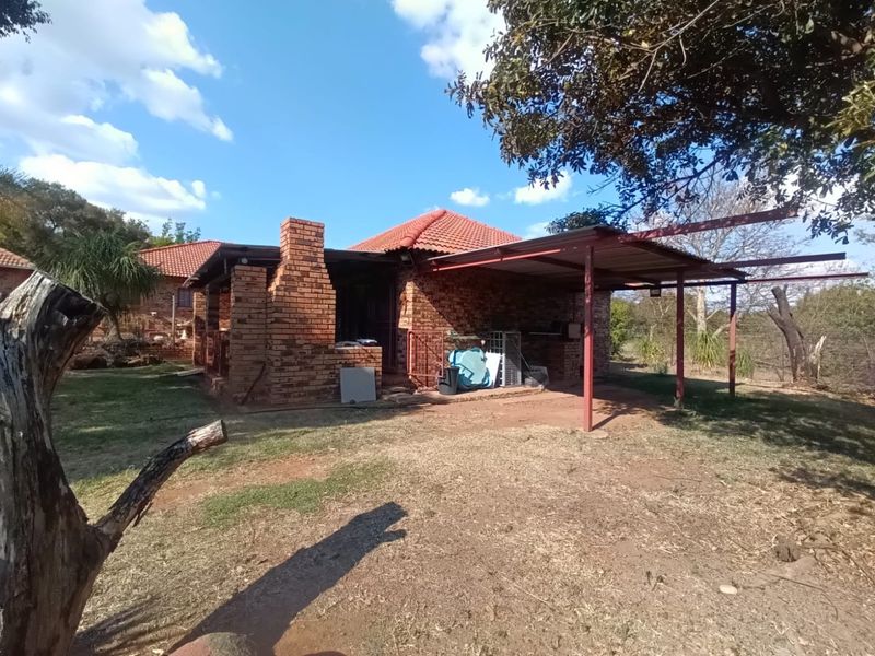 Rear view of a rustic brick farmhouse featuring a covered patio area with a built-in chimney and metal roof structure.