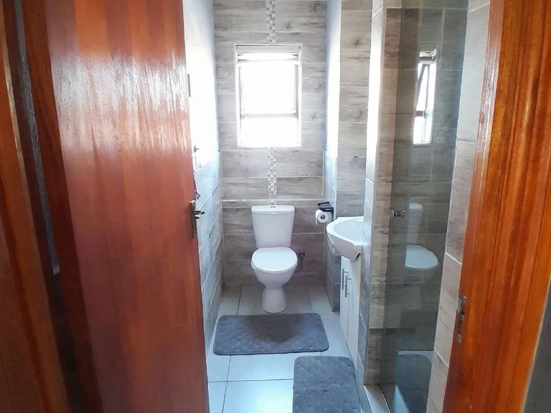 A compact, modern bathroom featuring tiled walls, a vanity basin, a toilet, and a glass-enclosed shower area.