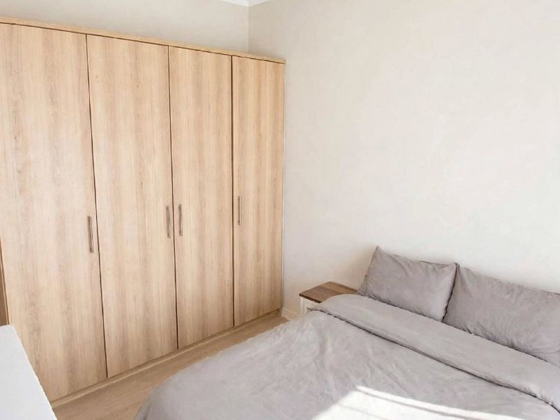 A bright and well-maintained bedroom featuring light wood-tone laminate flooring and a large, modern built-in wardrobe with ample storage space.