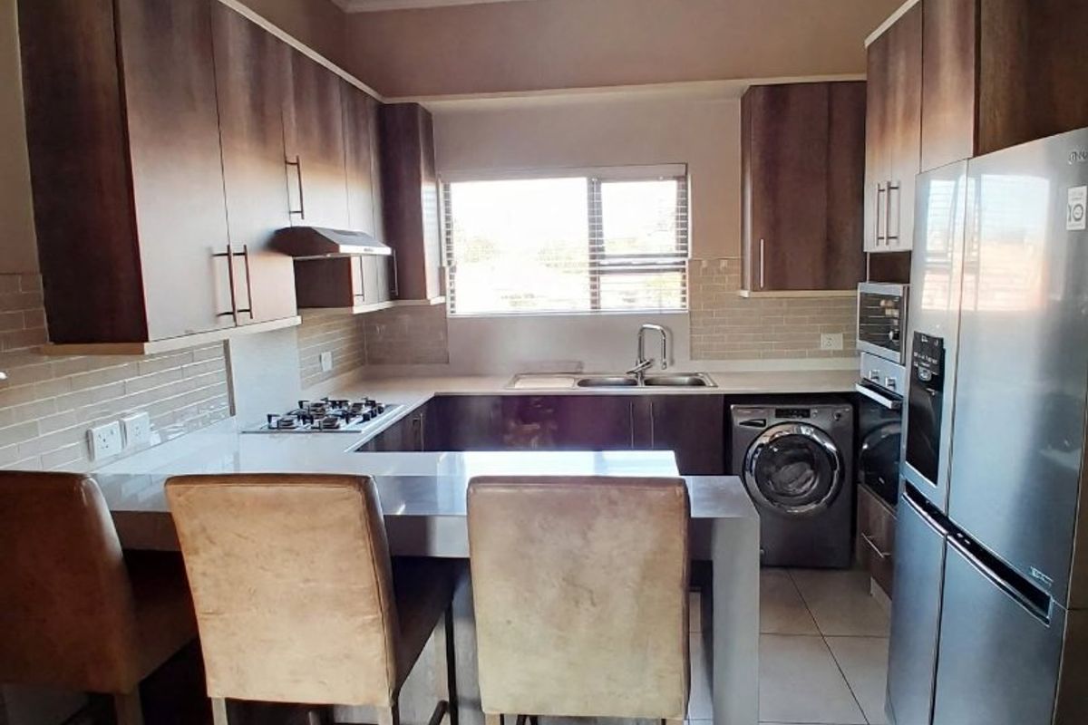 A functional kitchen featuring built-in cabinetry, a gas hob with extractor, under-counter oven, double sink, and a breakfast counter with tiled flooring.