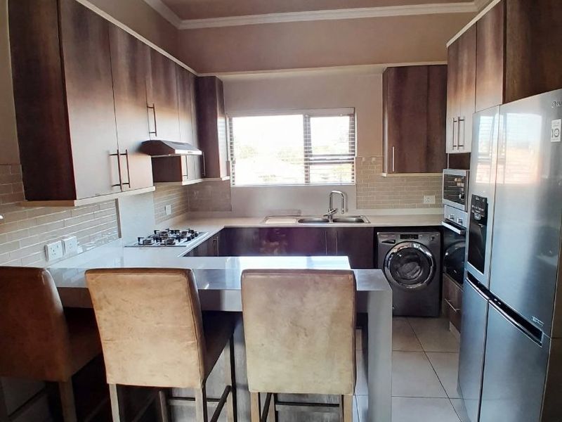 A functional kitchen featuring built-in cabinetry, a gas hob with extractor, under-counter oven, double sink, and a breakfast counter with tiled flooring.