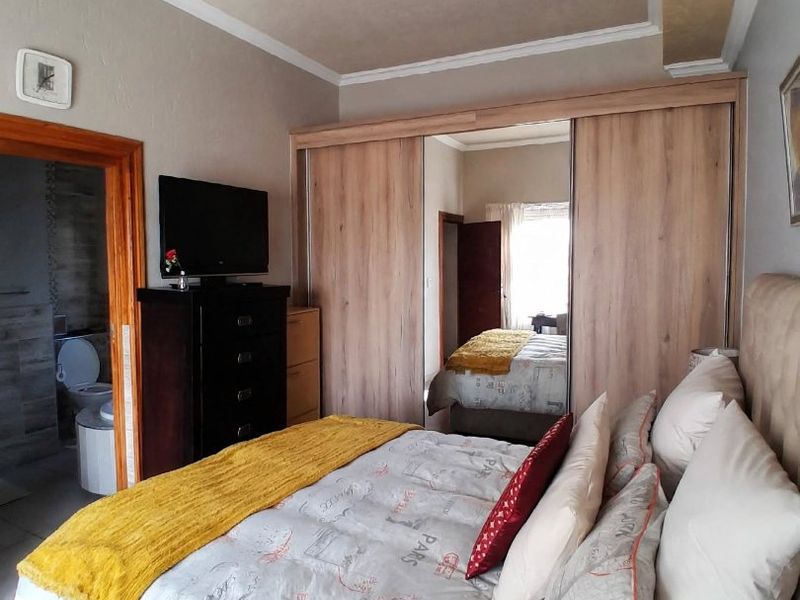 A bedroom featuring a built-in wardrobe with mirrored sliding doors, coved ceiling details, and laminate flooring, with an adjoining bathroom visible.