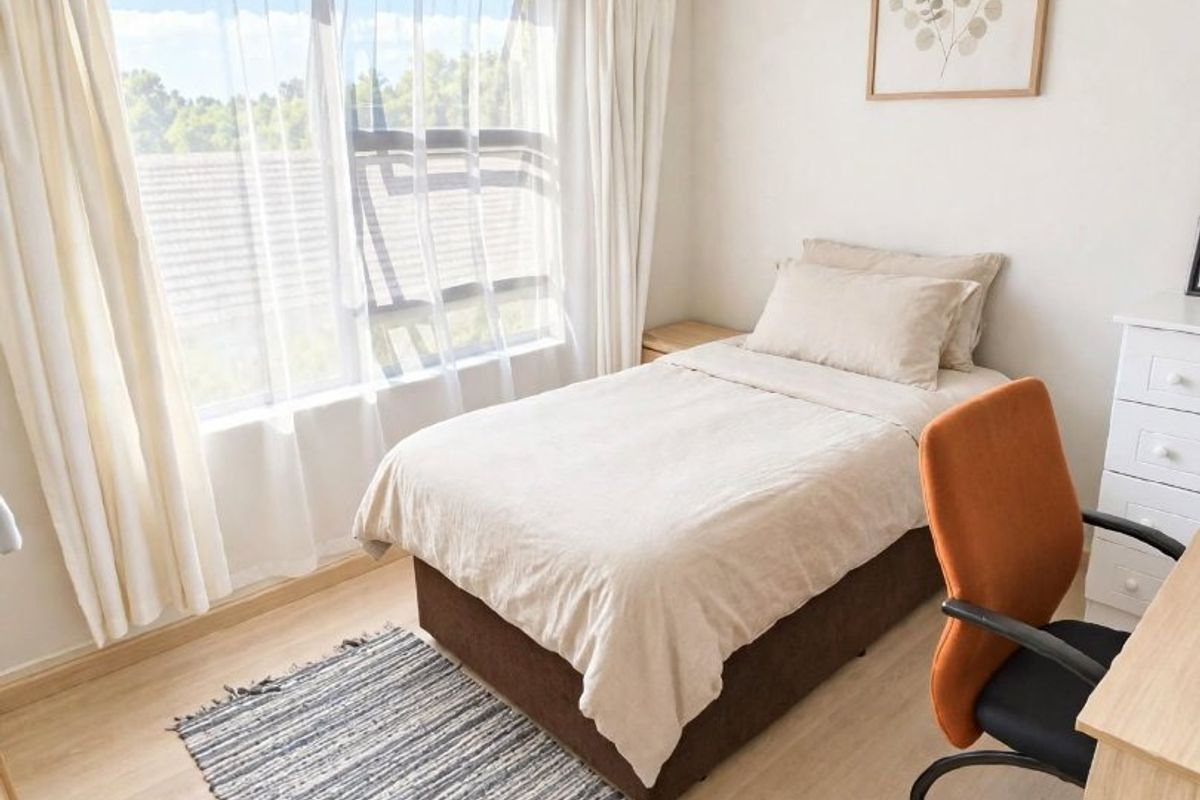 A bright and well-maintained bedroom featuring light-toned laminate flooring and a large sliding window that allows for ample natural light.