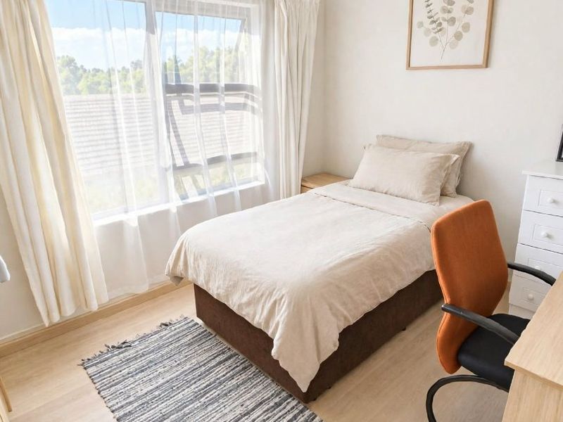 A bright and well-maintained bedroom featuring light-toned laminate flooring and a large sliding window that allows for ample natural light.