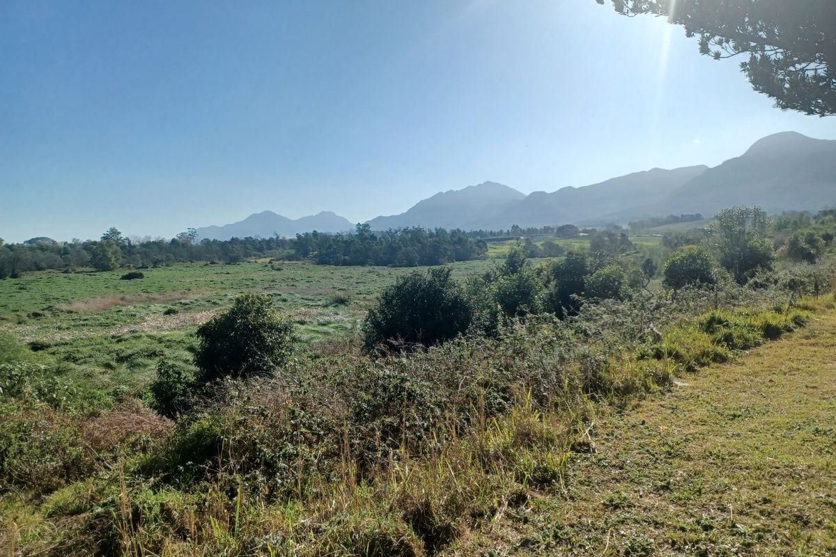 A scenic view of open residential land featuring expansive green fields and a distant mountain range under a clear sky.