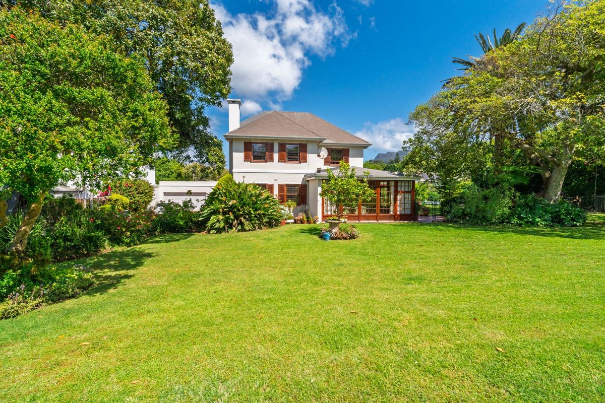 A well-maintained rear elevation of a two-story house featuring a spacious lawn, mature garden, and an enclosed patio area.