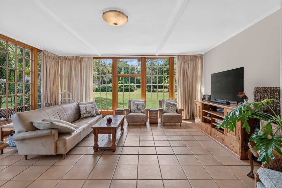 Spacious living room featuring large timber-framed windows with garden views, ceramic tiled flooring, and classic ceiling molding.