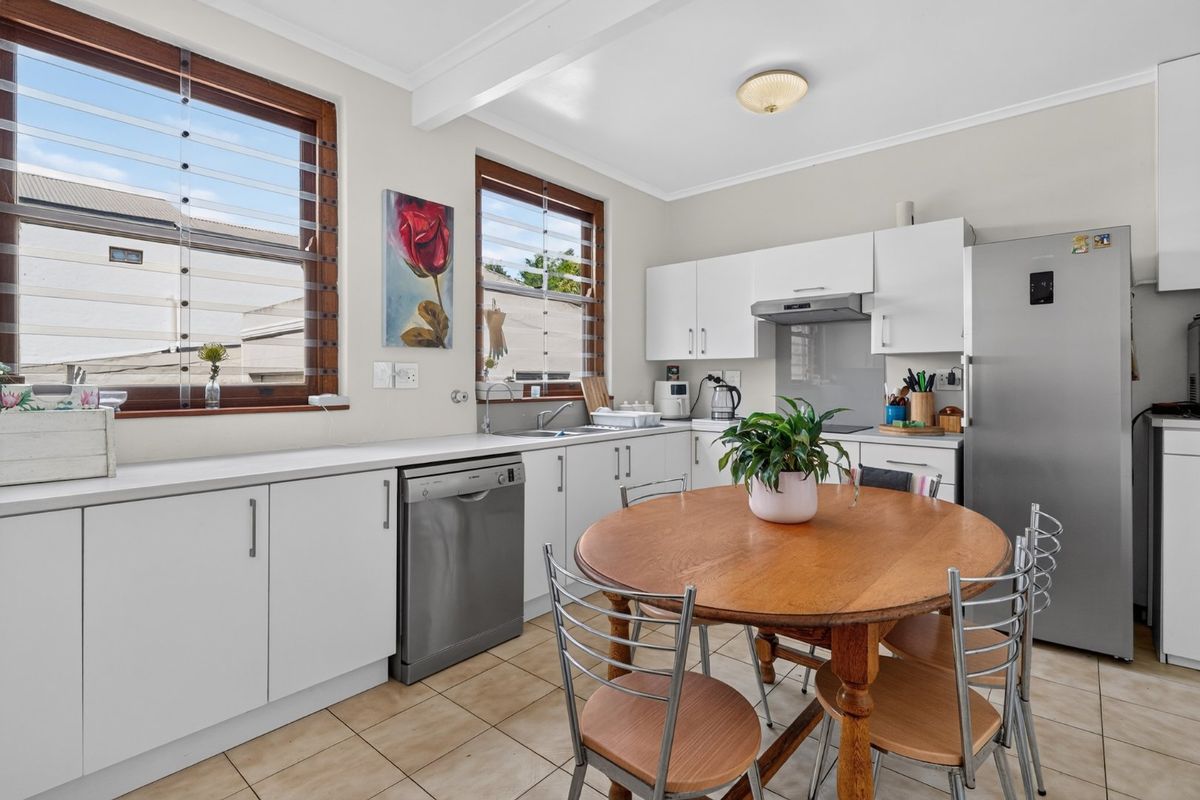 A functional kitchen featuring white cabinetry, laminate countertops, tiled flooring, and timber-framed louvre windows, providing a bright and practical cooking and dining space.