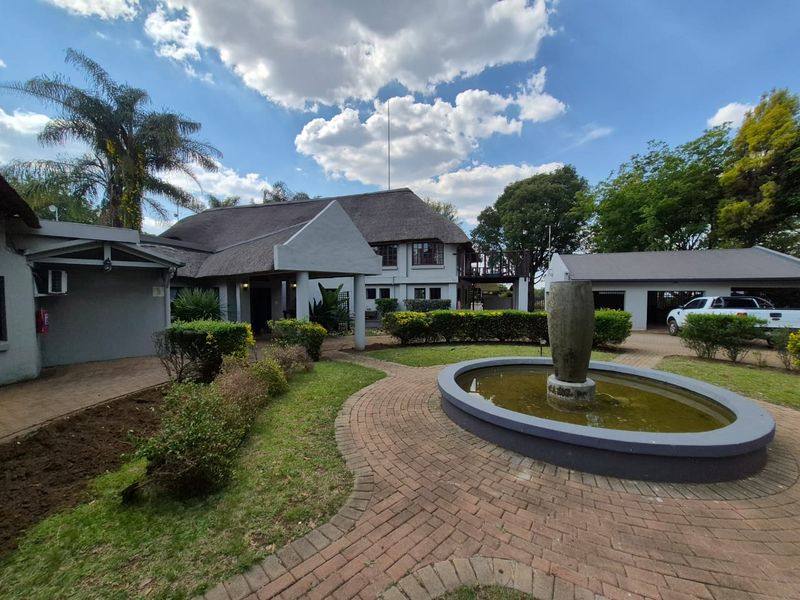 A well-maintained front exterior featuring a traditional thatched roof, a brick-paved courtyard with a central water fountain, and established garden landscaping.
