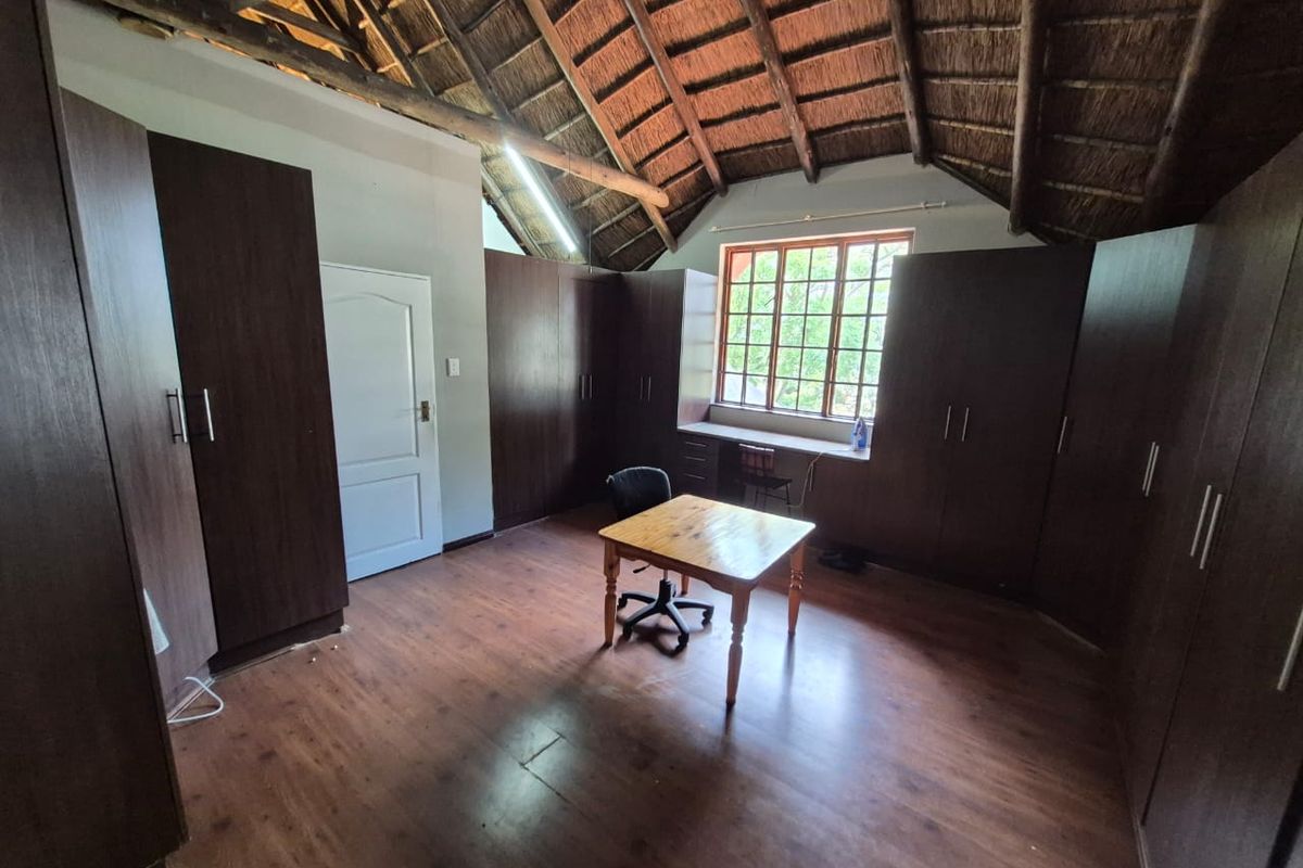 Spacious bedroom featuring a high exposed thatch ceiling, extensive built-in cabinetry, integrated desk space, and laminate flooring.