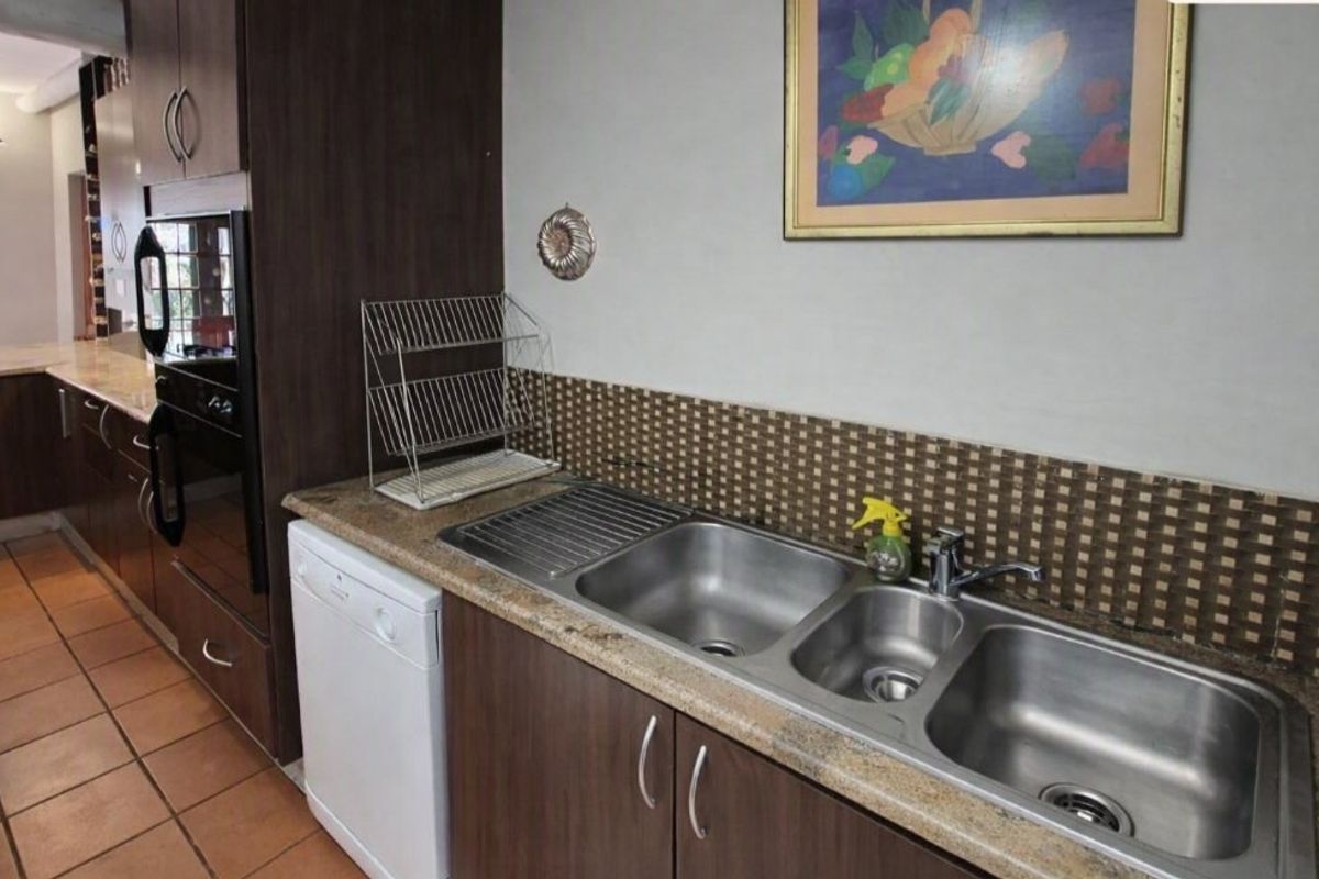 A functional kitchen featuring dark wood cabinetry, stone countertops, a triple stainless steel sink, and a mosaic tile backsplash with ceramic floor tiles.