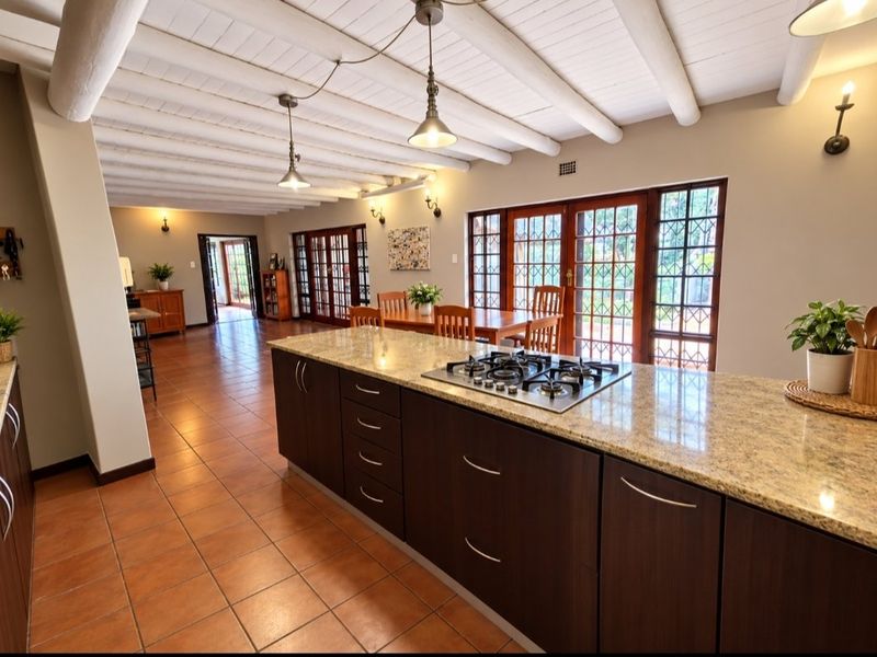 Spacious open-plan kitchen and dining area featuring a large granite island with a gas hob, exposed beam ceilings, and terracotta tiled flooring.