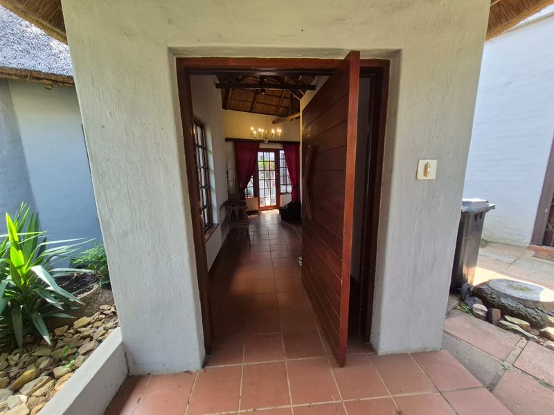 Entrance area featuring a timber door, tiled flooring, and a thatched roof structure, providing access to the interior living space.