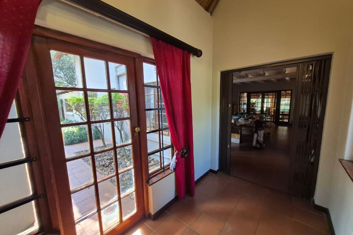 A living area featuring terracotta flooring, vaulted thatched ceilings, and timber-framed glass doors opening to an outdoor courtyard.