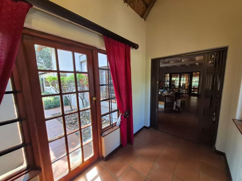 A living area featuring terracotta flooring, vaulted thatched ceilings, and timber-framed glass doors opening to an outdoor courtyard.