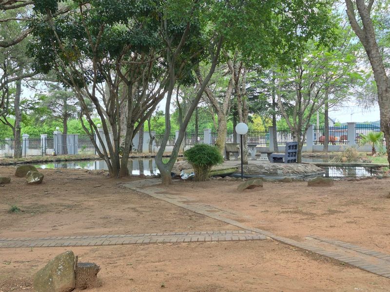 A spacious garden area featuring a central pond, mature trees, stone pathways, and secure perimeter fencing.