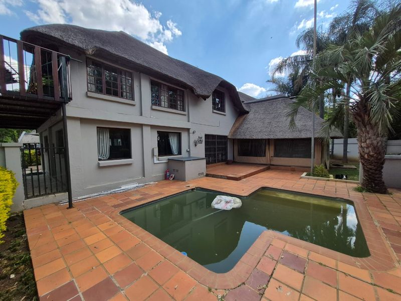 Rear exterior view of a two-story house with a thatched roof, featuring a swimming pool and a tiled patio area.