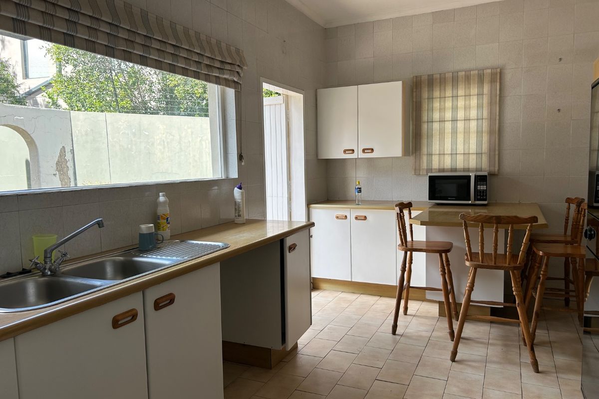 A functional kitchen featuring built-in cabinetry, a double bowl stainless steel sink, tiled splashbacks, and a breakfast counter area.