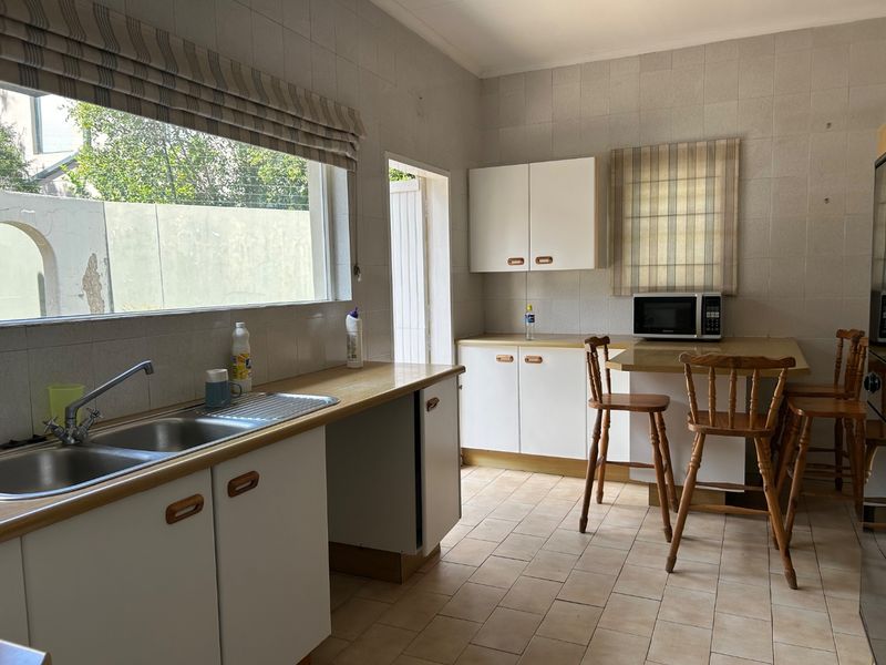A functional kitchen featuring built-in cabinetry, a double bowl stainless steel sink, tiled splashbacks, and a breakfast counter area.