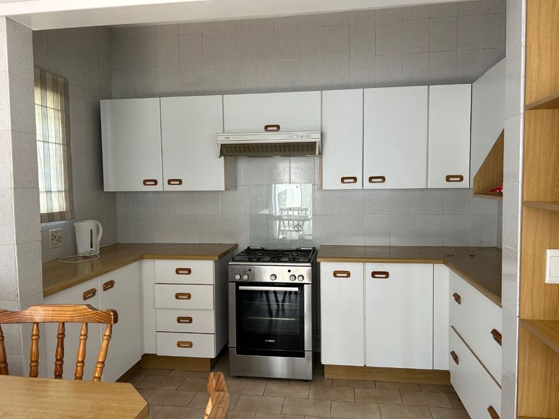A functional kitchen featuring white cabinetry, laminate countertops, a gas stove with extractor fan, and tiled finishes throughout.