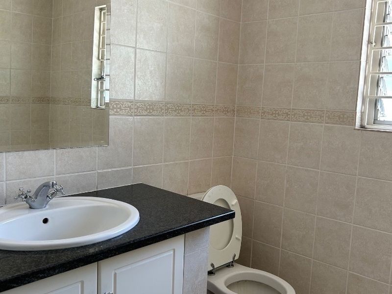 A clean, functional bathroom featuring a vanity with a granite countertop, ceramic wall and floor tiling, and a standard toilet.