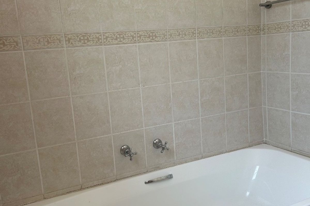 A functional bathroom featuring a built-in bathtub with wall-mounted chrome fixtures and neutral-toned wall tiling.