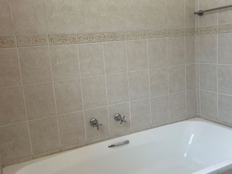 A functional bathroom featuring a built-in bathtub with wall-mounted chrome fixtures and neutral-toned wall tiling.