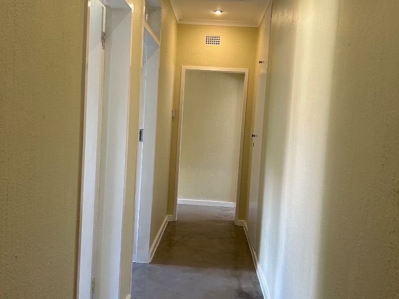 A vacant interior hallway featuring recessed downlights, a ceiling access hatch, and ventilation grilles, showing signs of wear on the flooring and walls.