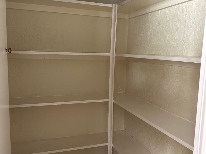 A functional walk-in pantry or storage area featuring built-in shelving and tiled flooring.