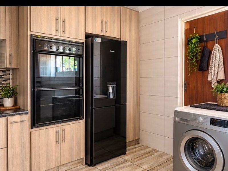 Modern kitchen featuring light wood-grain cabinetry, built-in double oven, tiled splashback, and neutral wall tiles, providing a clean and functional cooking space.