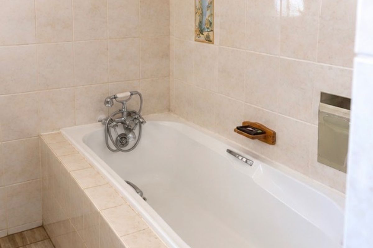 A clean, functional bathroom featuring a built-in bathtub with chrome fixtures and neutral ceramic wall and floor tiling.
