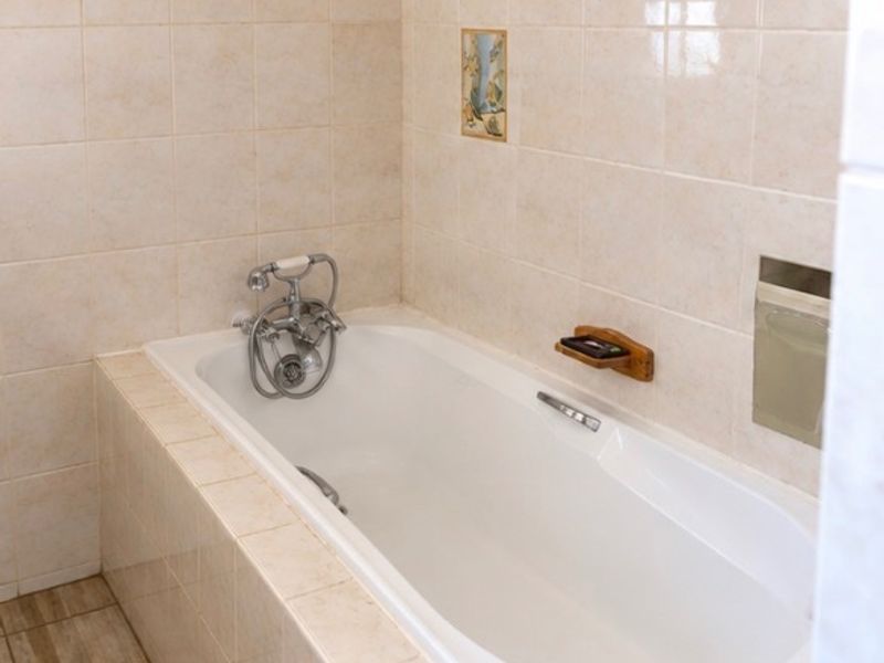 A clean, functional bathroom featuring a built-in bathtub with chrome fixtures and neutral ceramic wall and floor tiling.