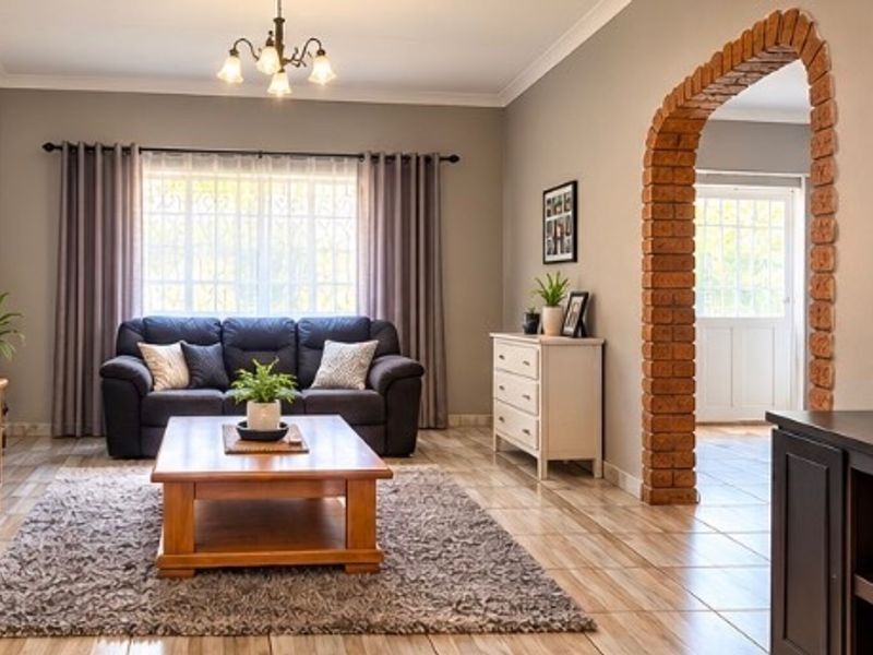 A well-maintained living room featuring tiled flooring, a distinctive brick archway leading to the entrance, and neutral wall tones.