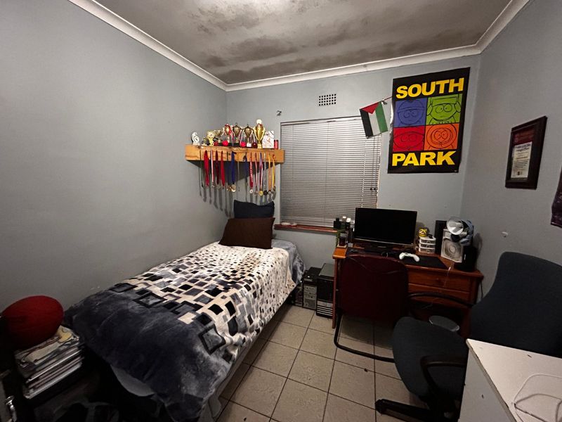 A compact bedroom featuring tiled flooring, venetian blinds, and a wall-mounted shelf. The ceiling shows visible signs of water staining.