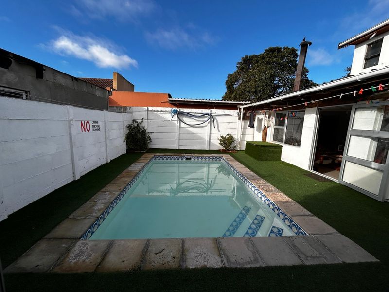 Outdoor pool area featuring a rectangular swimming pool with stone coping, surrounded by artificial grass and enclosed by a white precast concrete boundary wall.