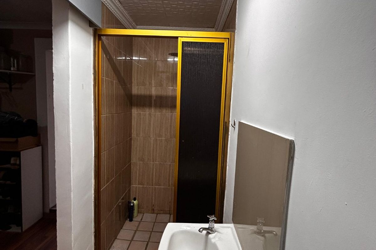A functional bathroom featuring a pedestal basin and a separate shower enclosure with tiled finishes and a textured ceiling.
