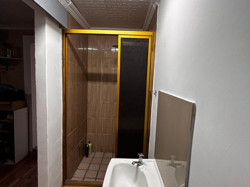 A functional bathroom featuring a pedestal basin and a separate shower enclosure with tiled finishes and a textured ceiling.