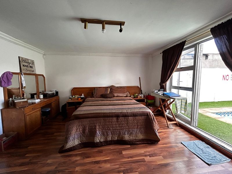 Spacious bedroom featuring warm laminate flooring, a built-in headboard, and large sliding glass doors providing direct access to the outdoor pool area.