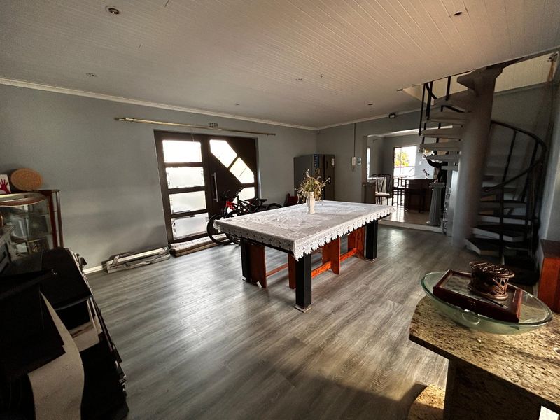 Spacious open-plan living area featuring modern laminate flooring, a distinctive spiral staircase, and a timber panelled ceiling with recessed lighting.