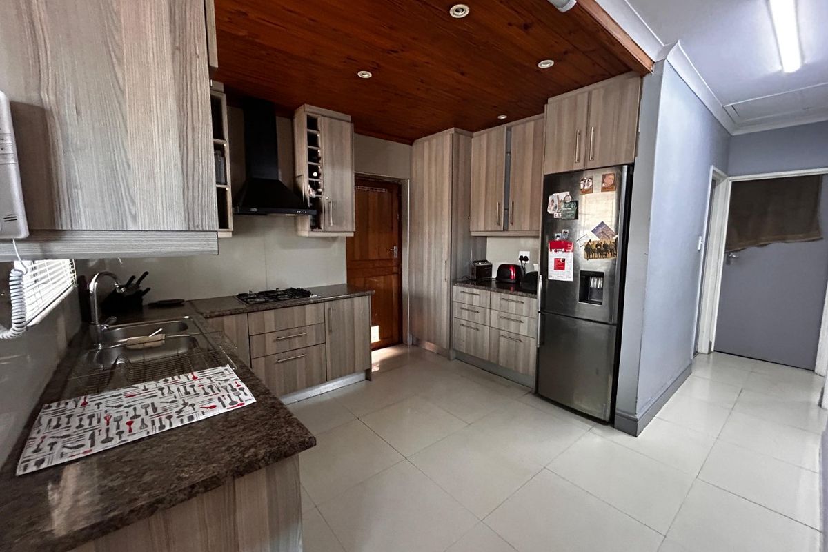 A functional kitchen featuring wood-look cabinetry, granite countertops, a gas hob with extractor fan, and a distinctive timber ceiling.