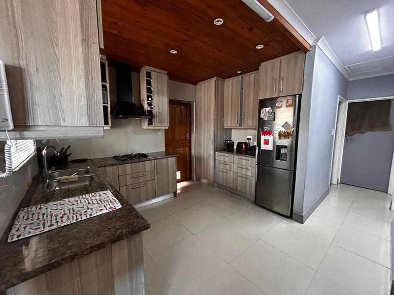 A functional kitchen featuring wood-look cabinetry, granite countertops, a gas hob with extractor fan, and a distinctive timber ceiling.